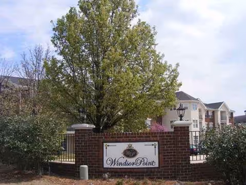 Front entrance of Windsor Point senior living with brick sign, gate, and trees.