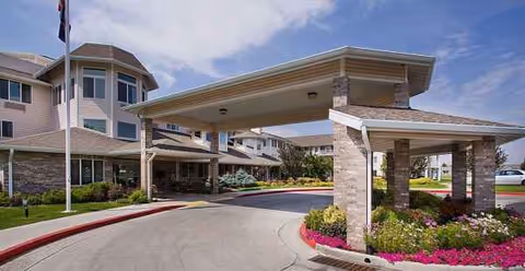 Senior living facility entrance featuring a covered drive, stone columns, and landscaped approach.