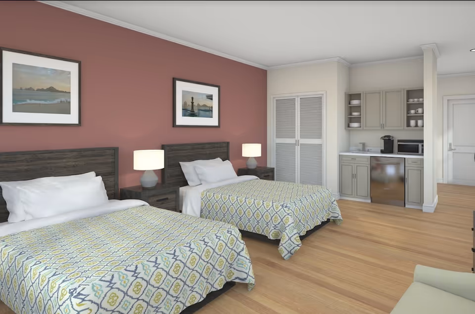 A spacious assisted-living bedroom with two beds, bedside tables and lamps, framed artwork, and a small kitchenette area.