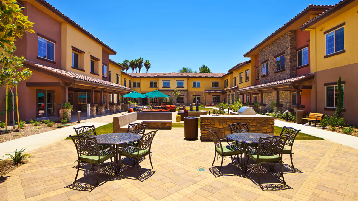 Sunny central outdoor courtyard with metal patio tables and chairs, umbrellas, seating areas and surrounding two-story buildings.