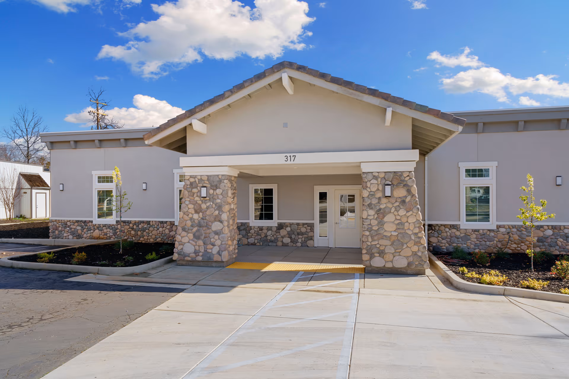 Front entrance of a single-story stone-and-stucco senior living building with a covered porch, double doors, and the number 317 above the entry.