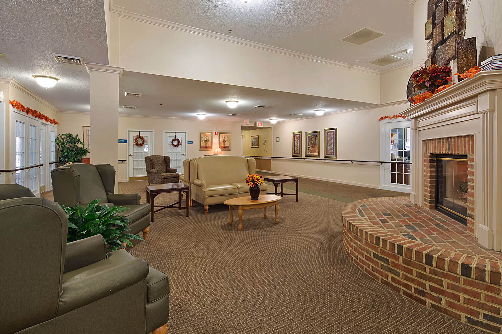 Spacious senior living lounge with sofas, armchairs, coffee tables, plants, and a brick fireplace.