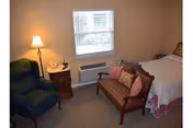 Cozy bedroom in a senior living facility with a bed, seating, and a window.