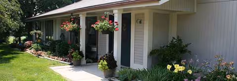 A single-story senior living facility exterior with hanging flower baskets by the entrance.