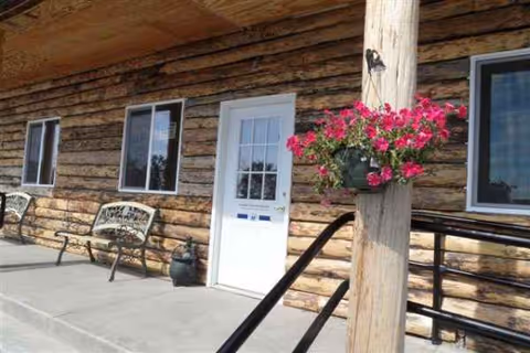 Exterior view of a log-style senior living facility entrance with benches and flowers.