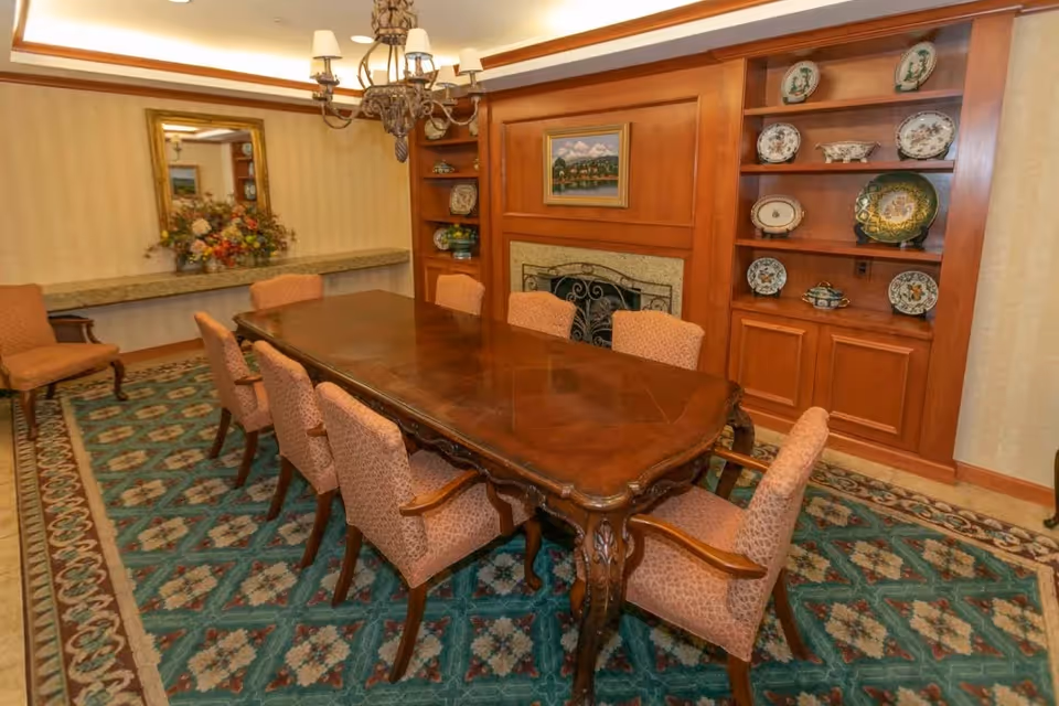 Formal dining room with a long wooden table surrounded by upholstered chairs, a chandelier, built-in shelving displaying plates, and a fireplace.