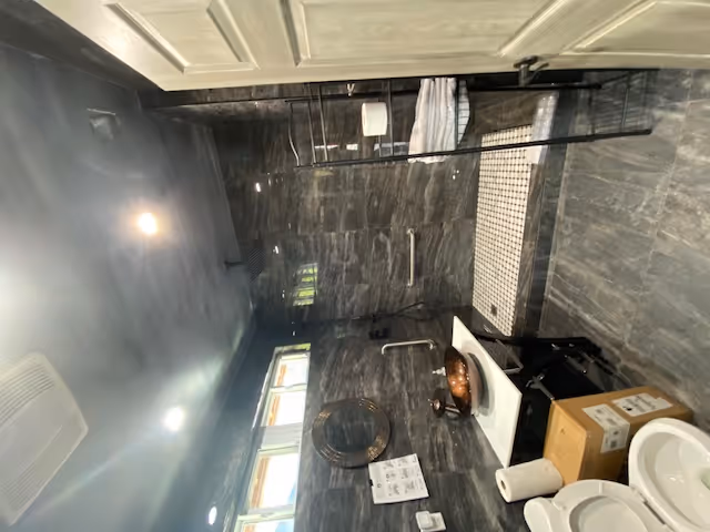 Modern bathroom with dark gray marble walls, a walk-in tiled shower, vanity with a vessel sink, toilet, and boxes on the floor.