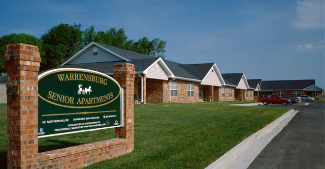 Exterior view of Warrensburg Senior Apartments with a green sign, brick buildings, and a neatly mowed lawn.