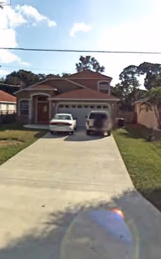 Two-story stucco house with a long concrete driveway and two vehicles parked in front of a double garage.