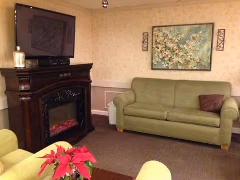 A cozy living room in Meadow Wind Health Care Center with a sofa, fireplace, and TV.