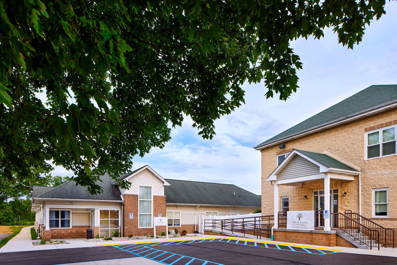 Exterior view of The Seasons of Saxonburg facility with entrance, walkway, and parking.