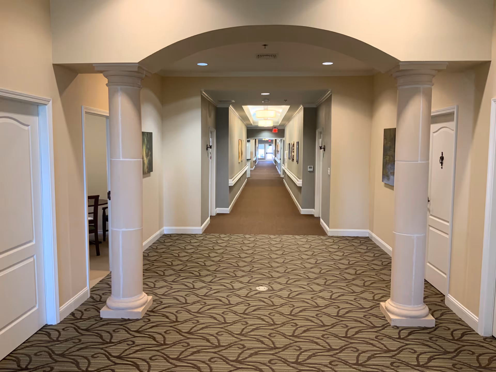 A long carpeted interior hallway with decorative columns, doors on both sides, and framed artwork along the walls.