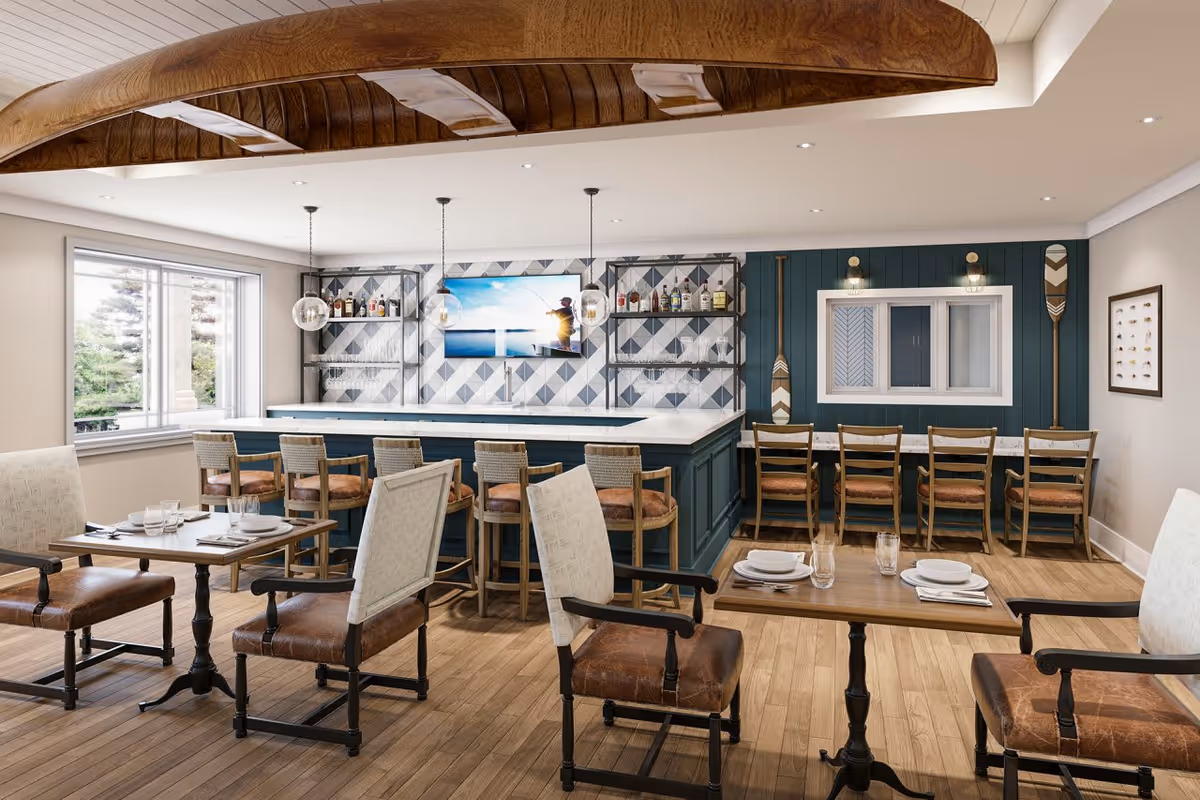 A cozy dining area with wooden floors and a large window letting in natural light. The room features a bar with stools, shelves with bottles and glasses, and a television mounted on a patterned wall. There are several tables with chairs set for dining, and decorative wooden paddles on the wall.