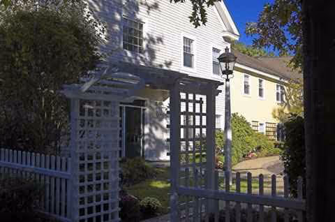 A white two-story building with a lattice archway gate and manicured landscaping at the entrance.