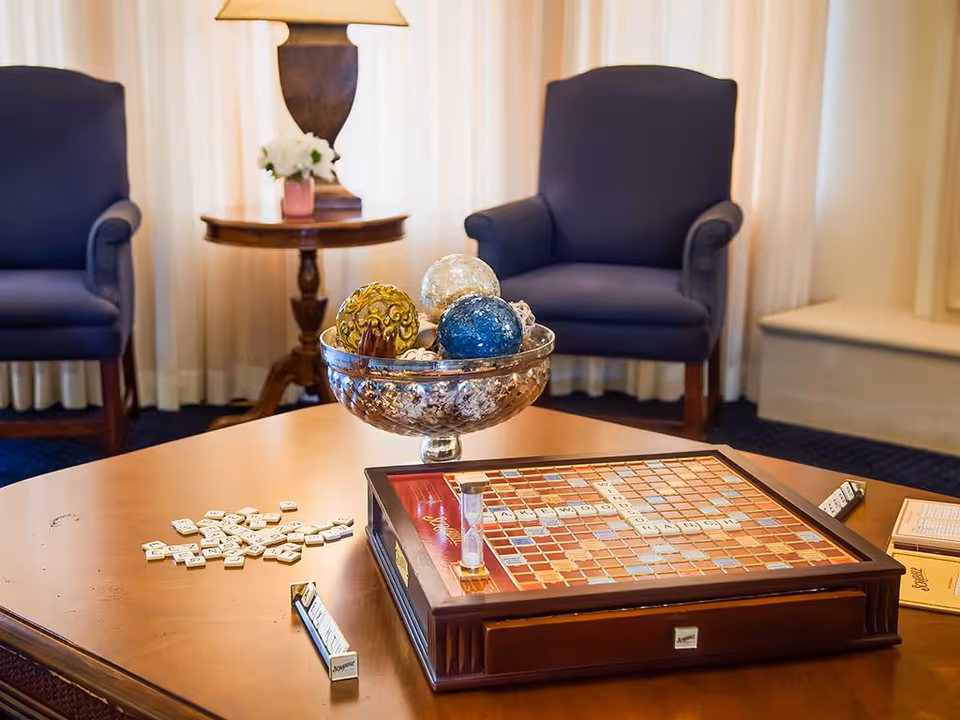 A cozy sitting area with two upholstered armchairs, a lamp on a side table, and a coffee table displaying a Scrabble board and a decorative bowl of ornaments.