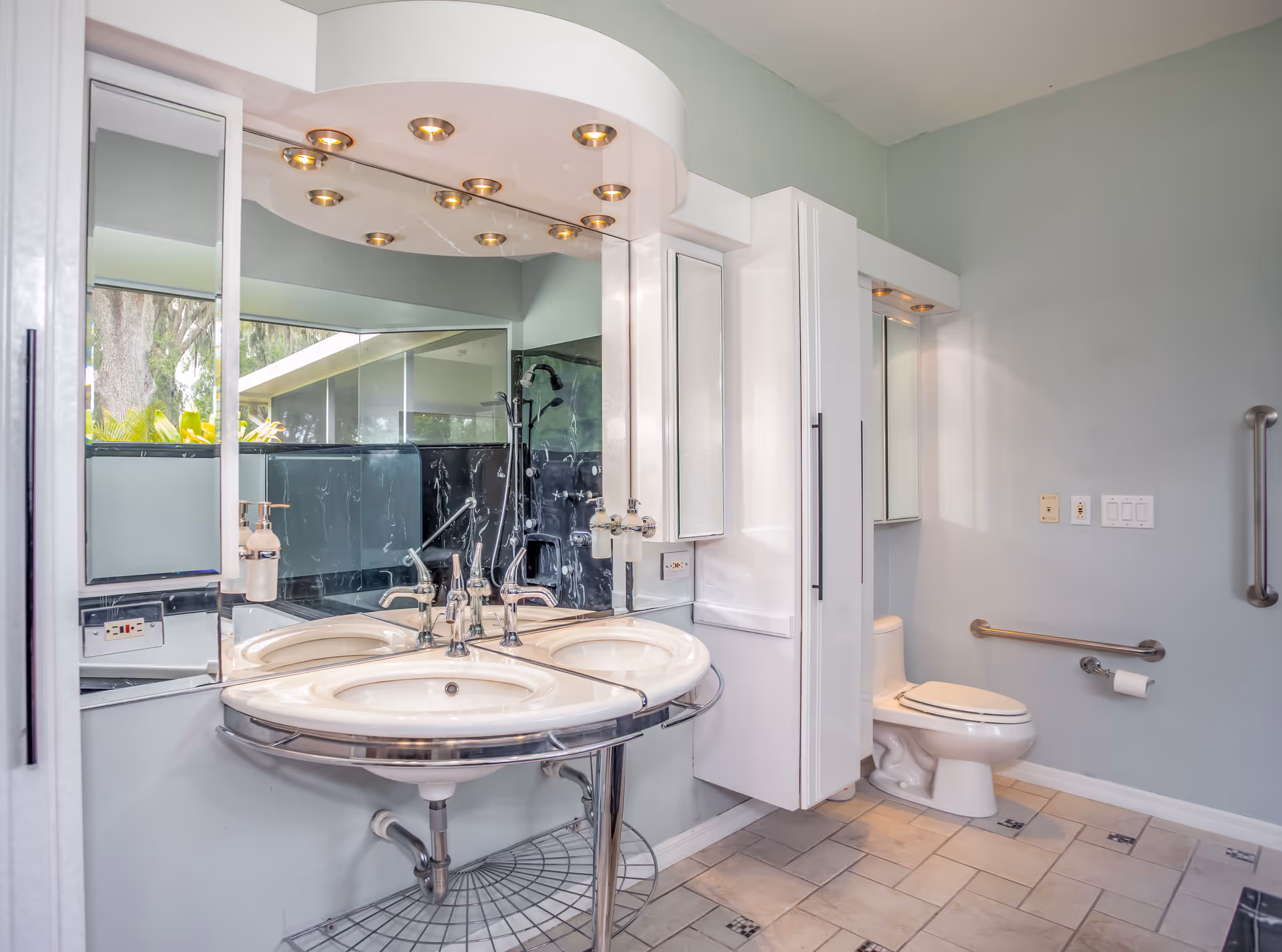 Accessible bathroom with a double sink and chrome fixtures, large mirrored vanity, toilet with grab bars, and tiled tile floor.