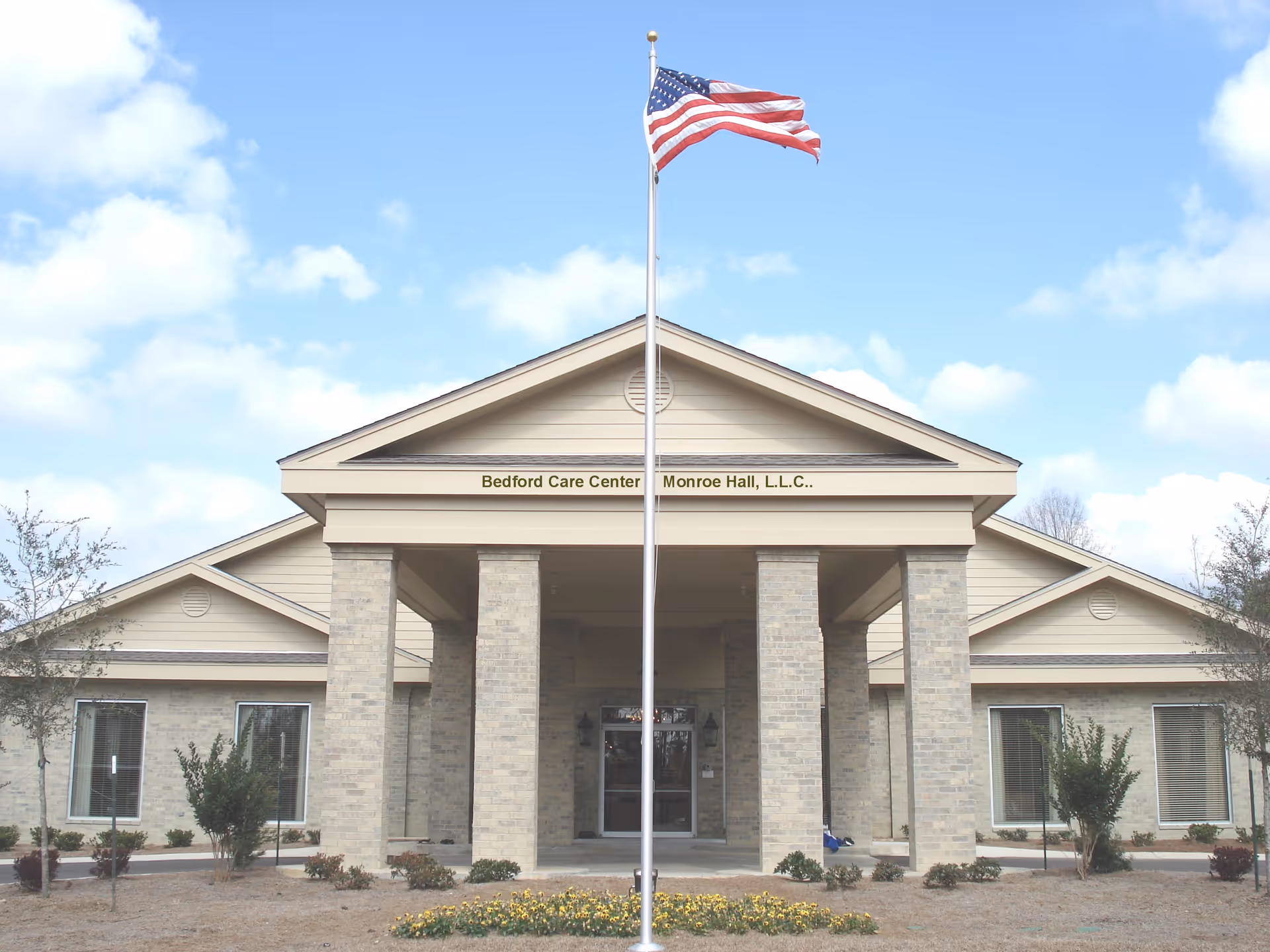 Front entrance of Bedford Care Center–Monroe Hall with an American flag on a flagpole in front.
