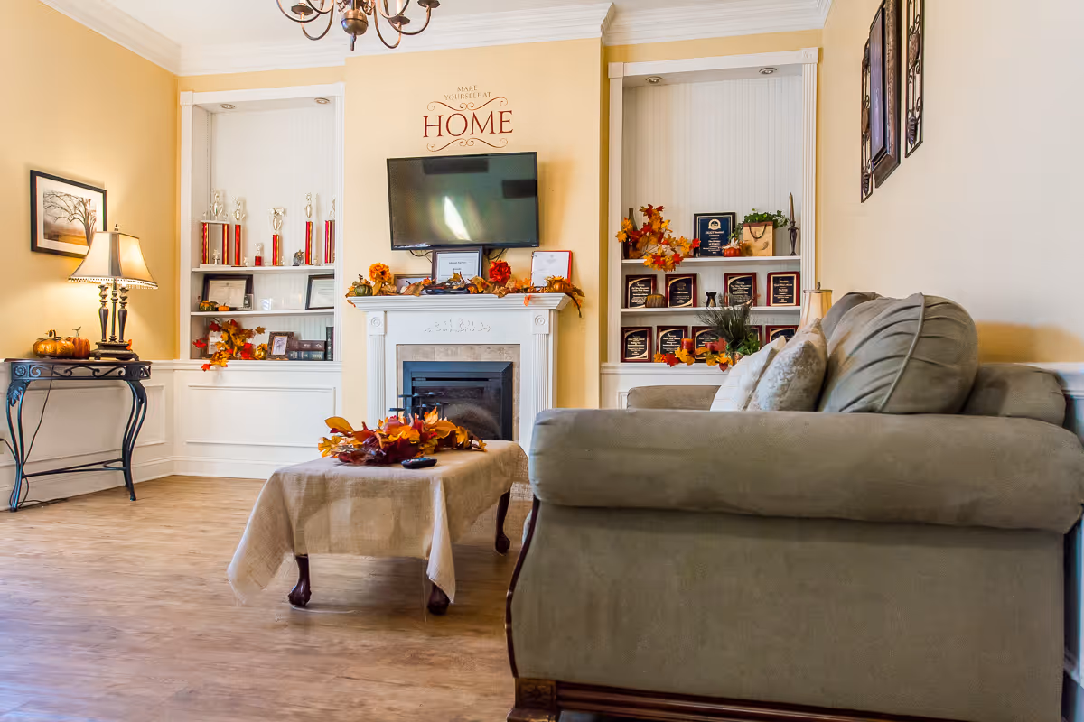 Cozy living room with a sofa, coffee table, fireplace, wall-mounted TV and built-in shelves decorated with fall accents and awards.