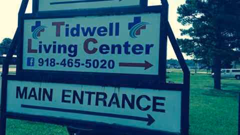 Outdoor sign reads Tidwell Living Center main entrance with arrows on a grassy area