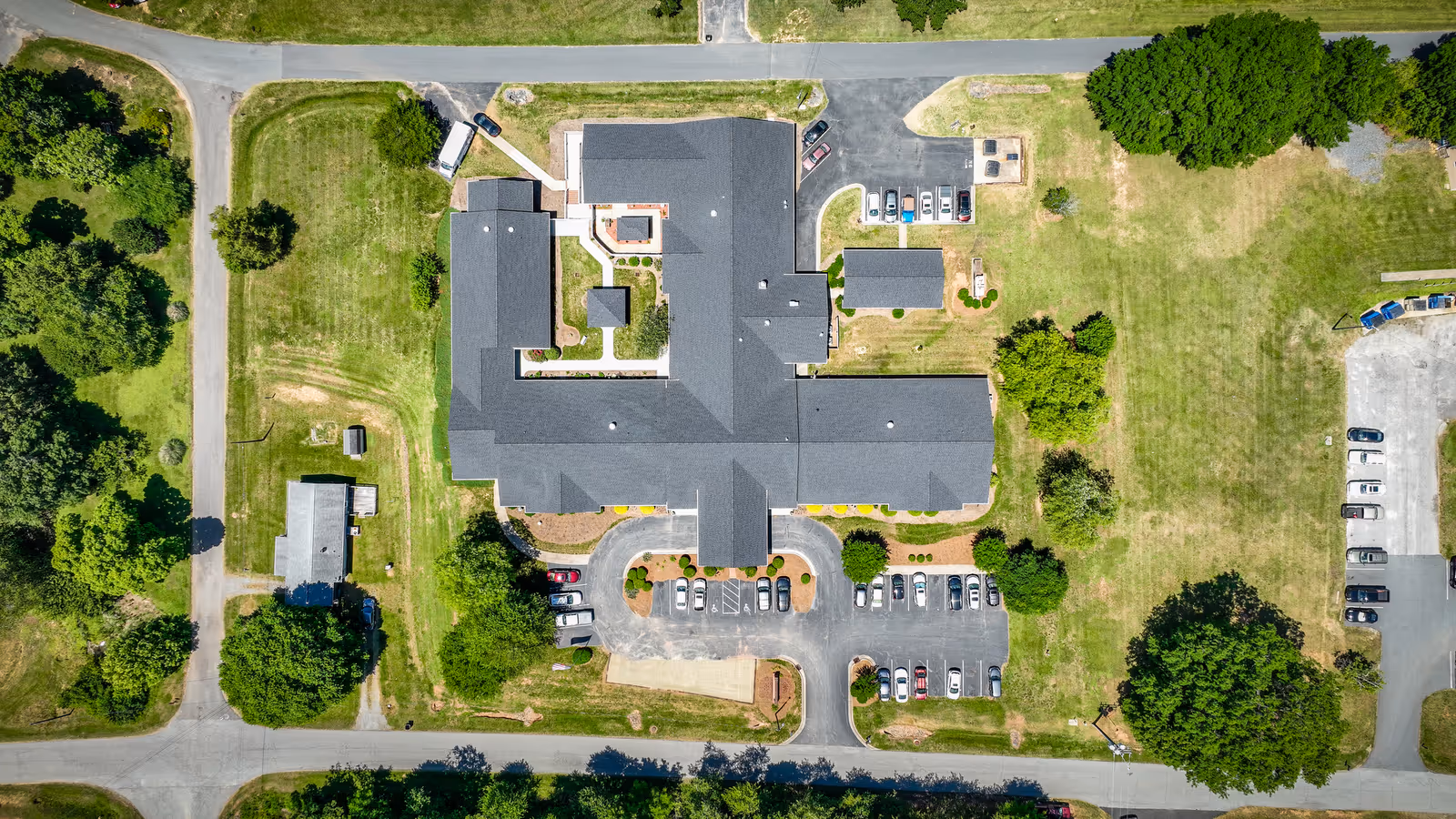 Aerial view of Walnut Ridge Assisted Living facility showing the building with a dark roof, surrounding parking lots with cars, green lawns, trees, and adjacent roads.