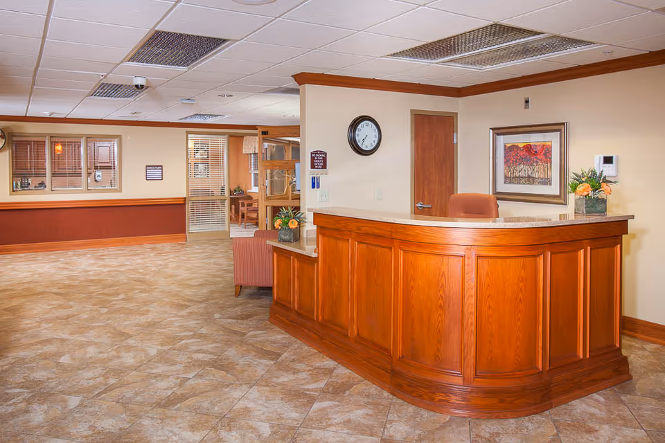 A reception lobby with a curved wooden front desk, clock on the wall, seating and tiled floor.