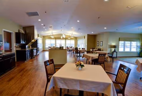 Interior dining room with several tables set with white tablecloths and chairs.
