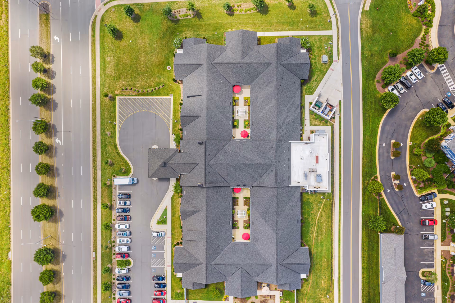 Aerial top-down view of the Morningside House of Fredericksburg building with parking lots, roads, courtyards featuring red umbrellas, and landscaped grounds.