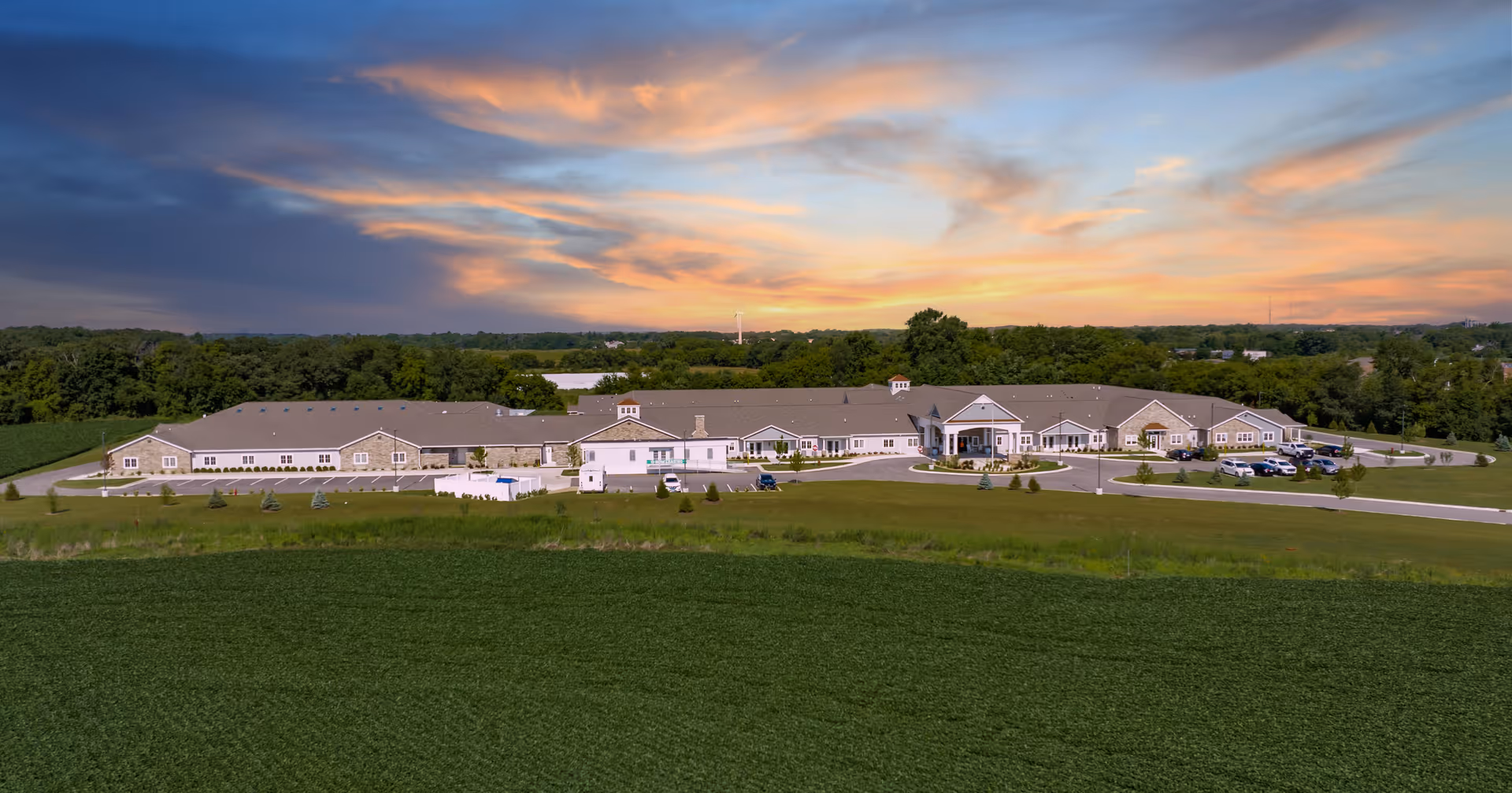 Wide exterior view of the Cedarhurst of Woodstock senior living building set against a colorful sunset sky.