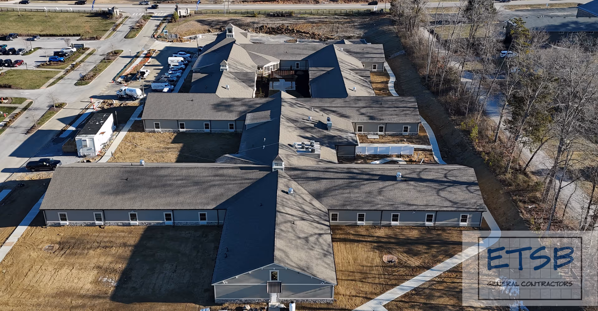 Aerial view of a single-story senior living facility with multiple winged buildings, parking area, and surrounding trees.
