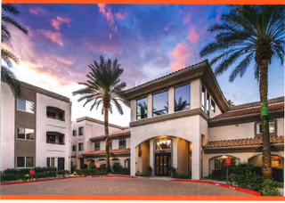 Exterior view of The Ranch Estates At Scottsdale building at sunset with palm trees and a driveway in front.
