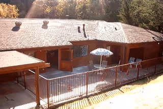 Sunlit exterior of a single-story lodge showing a fenced patio with an umbrella table and chairs.