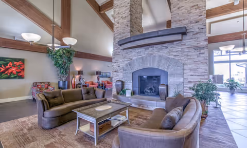 Common lounge area with sofas and armchairs arranged around a large stone fireplace under exposed wooden beams.