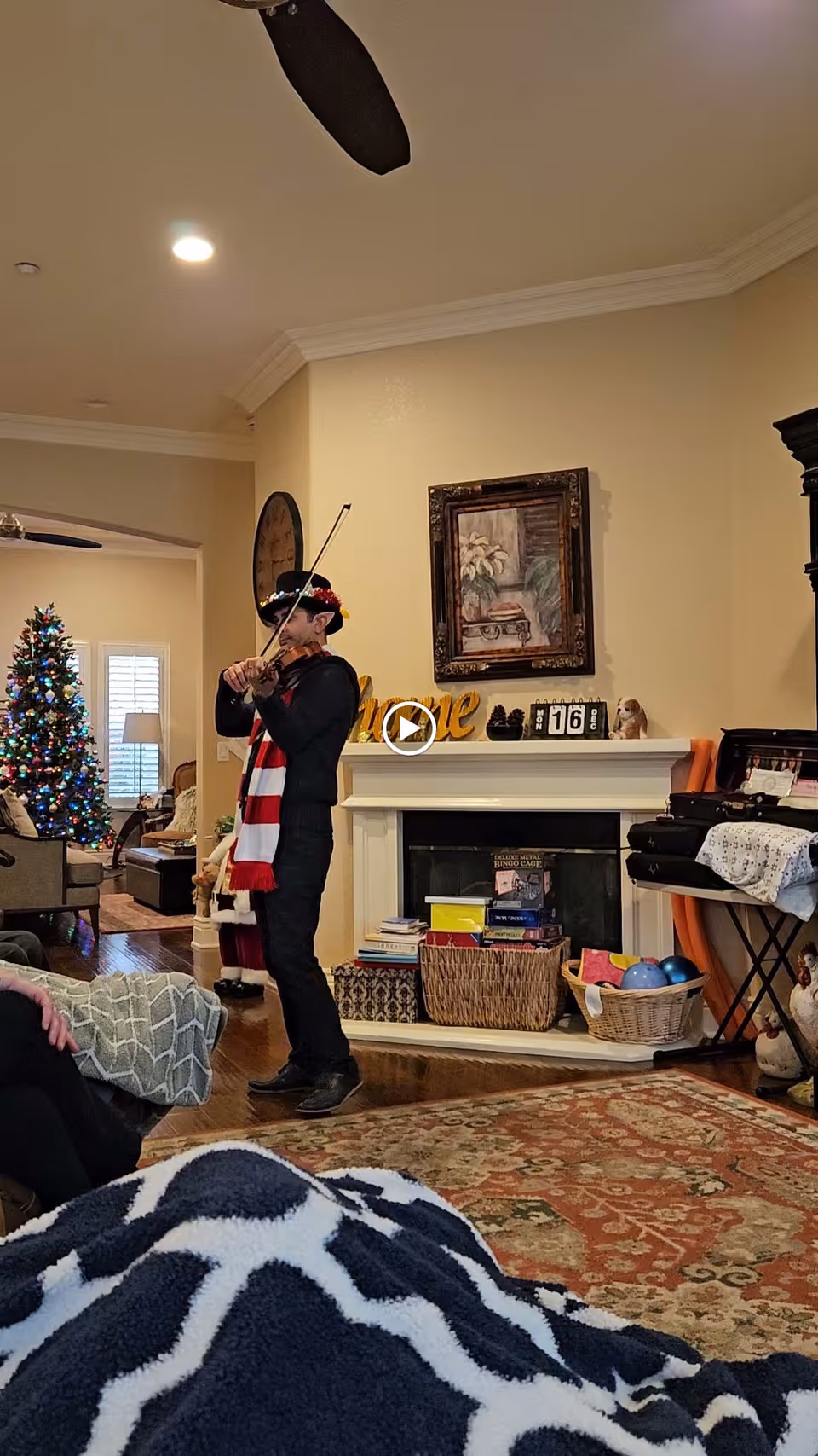 A person playing a violin in a decorated living room with a fireplace and a Christmas tree.