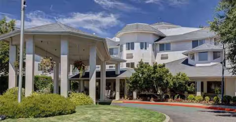 Modern senior living facility with a covered entrance, drive, and landscaped front yard.