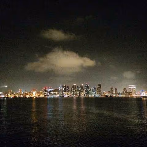 Nighttime city skyline across a calm bay with illuminated buildings along the horizon.