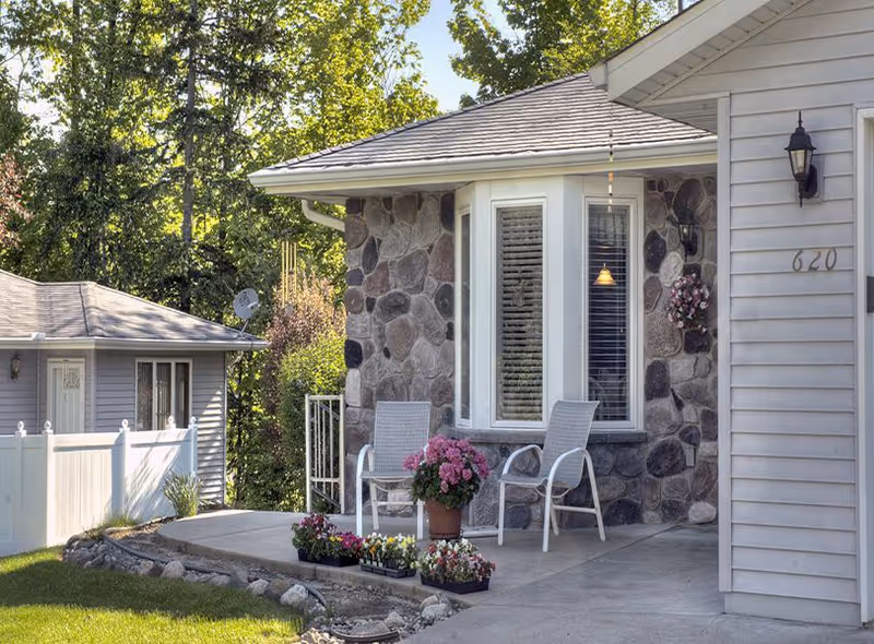 Front porch of a stone-faced house with two white chairs, potted flowers, and the house number 620 visible next to the door.