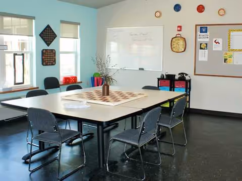 Well-lit activity room featuring a large table, chairs, a whiteboard, and a bulletin board.