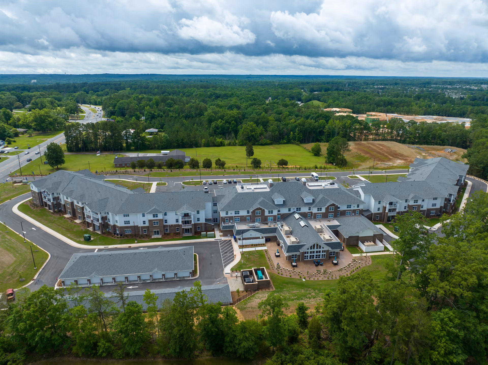 Aerial view of Greenway Square Retirement Community, a large multi-wing building surrounded by greenery and parking areas under a cloudy sky.