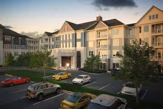 Exterior view of a multi-story residential building at dusk with several parked cars in the parking lot and trees around the area.