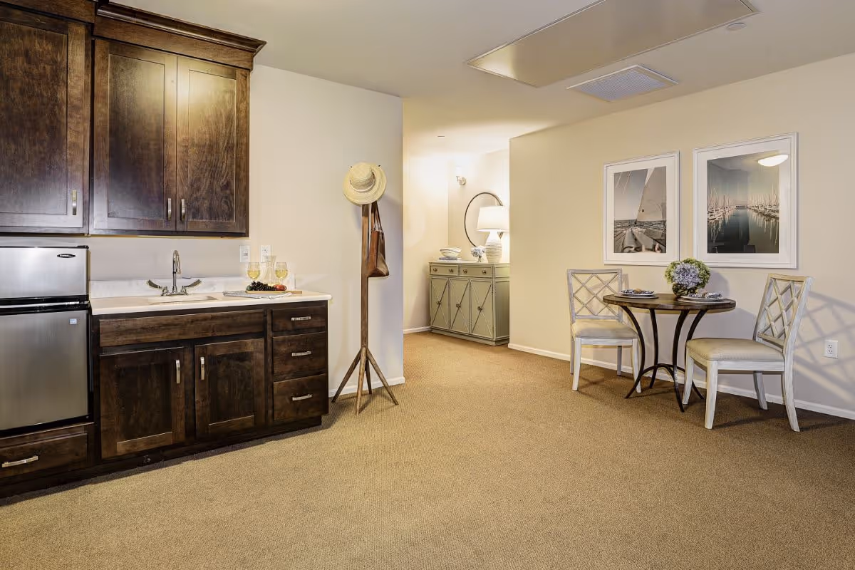 Open studio-style room with a dark wood kitchenette on the left and a small round dining table with two chairs on the right.