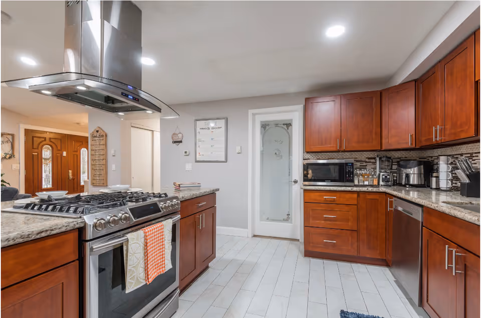 Modern kitchen with a stainless steel range and hood, granite countertops and cherry wood cabinets.