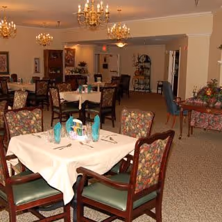 Dining room with multiple set tables, floral-upholstered chairs, chandeliers and a buffet/display area.