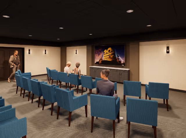 Small screening room with rows of blue upholstered chairs facing a wall-mounted screen, three people seated and one person standing near the back.