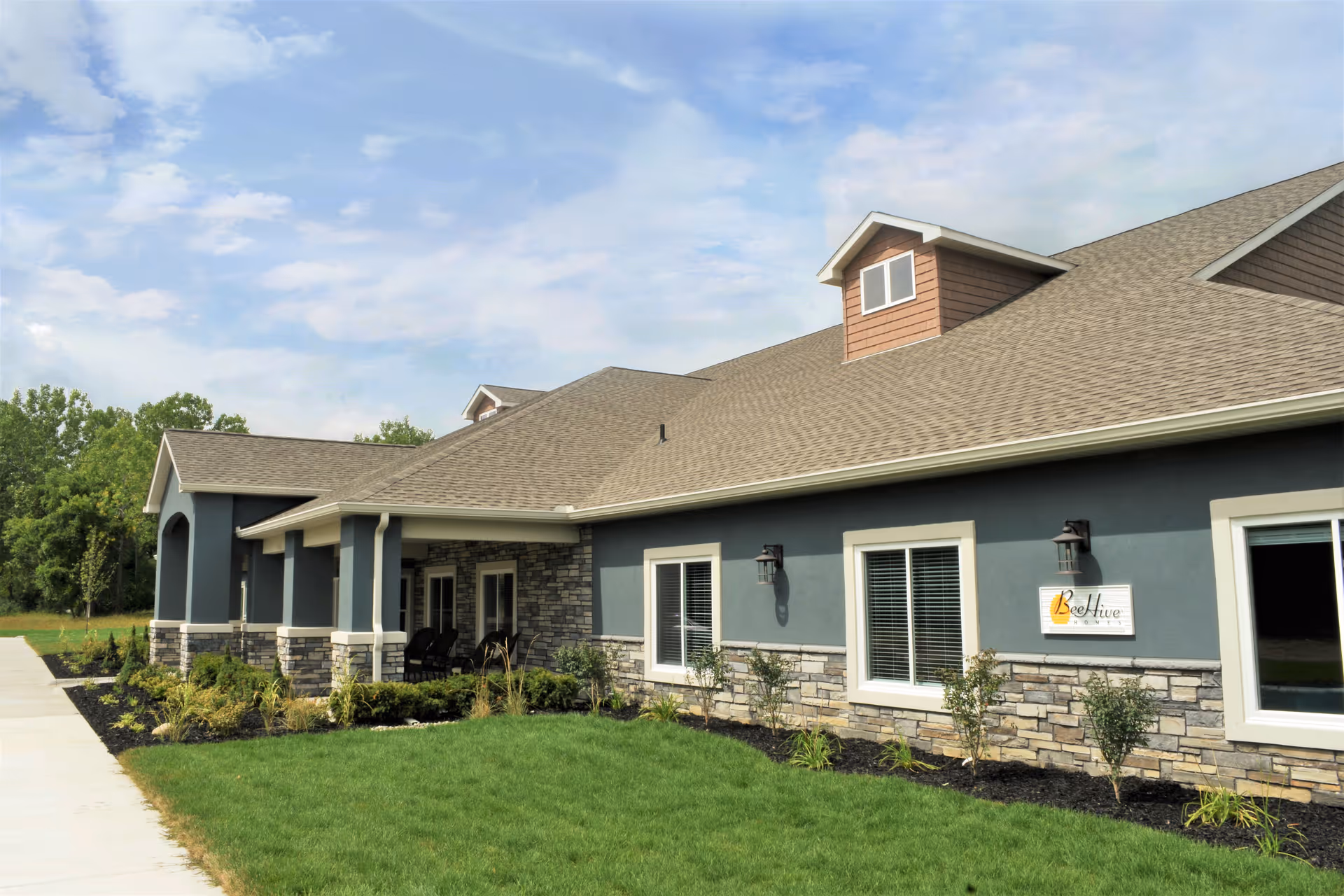 Front exterior of a single-story BeeHive Homes senior living building with a covered entrance, stone accents and landscaped lawn.